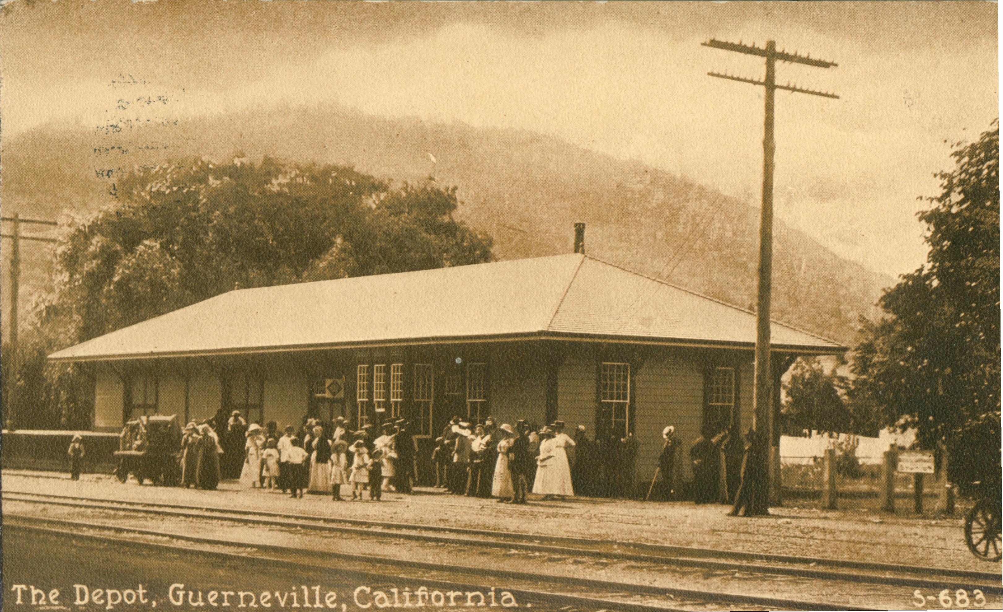 Shows a number of people standing outside of the railroad depot